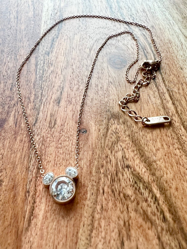 K&ouml;nnte beinhalten: Eine goldene Kettenkette mit einem klaren Kristall-Mickey-Mouse-Anh&auml;nger.