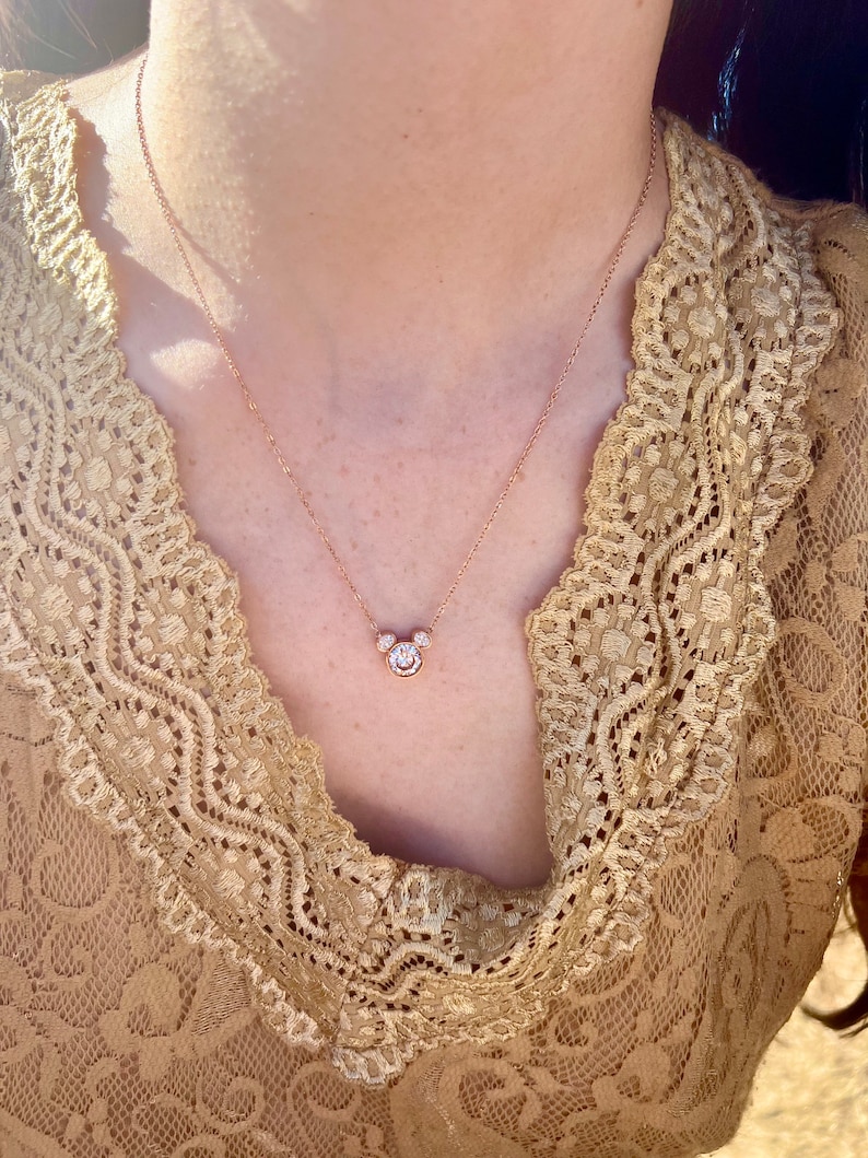 K&ouml;nnte beinhalten: Eine zarte goldene Kettenkette mit einem kleinen, funkelnden Diamant-Mickey-Mouse-Anh&auml;nger.