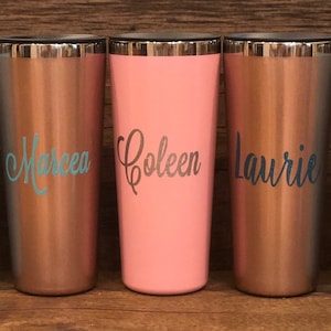 May include: Five stainless steel travel mugs with personalized names: Lindsey, Marcea, Coleen, Laurie, and Trudy. The mugs are in various colors: light blue, copper, pink, and teal.