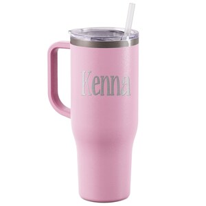 K&ouml;nnte beinhalten: Ein hellrosa isolierter Becher mit Henkel und transparentem Deckel. Auf dem Becher ist der Name "Kenna" eingraviert. Ein klarer Strohhalm ist in den Deckel gesteckt.