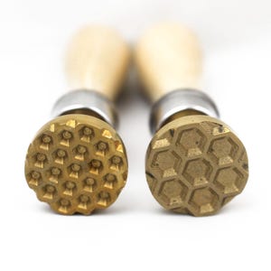 May include: Two wooden handled metal stamps with hexagonal patterns. The stamps are used for creating impressions in clay or wax.