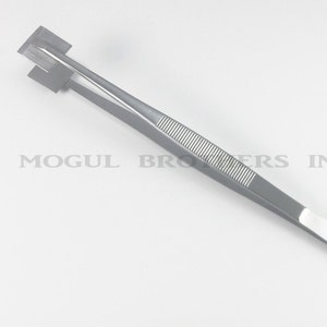 Könnte beinhalten: Eine silberfarbene Pinzette mit einem strukturierten Griff und einer quadratischen Spitze. Die Pinzette ist mit "Mogul Bros. Stainless" beschriftet.