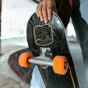 May include: A black skateboard with orange wheels. A sticker on the board features a pirate-themed design with the text "Yo Ho. All together, Hoist the colours high, Heave Ho, Thieves and Beggary Never Shall We Die!"