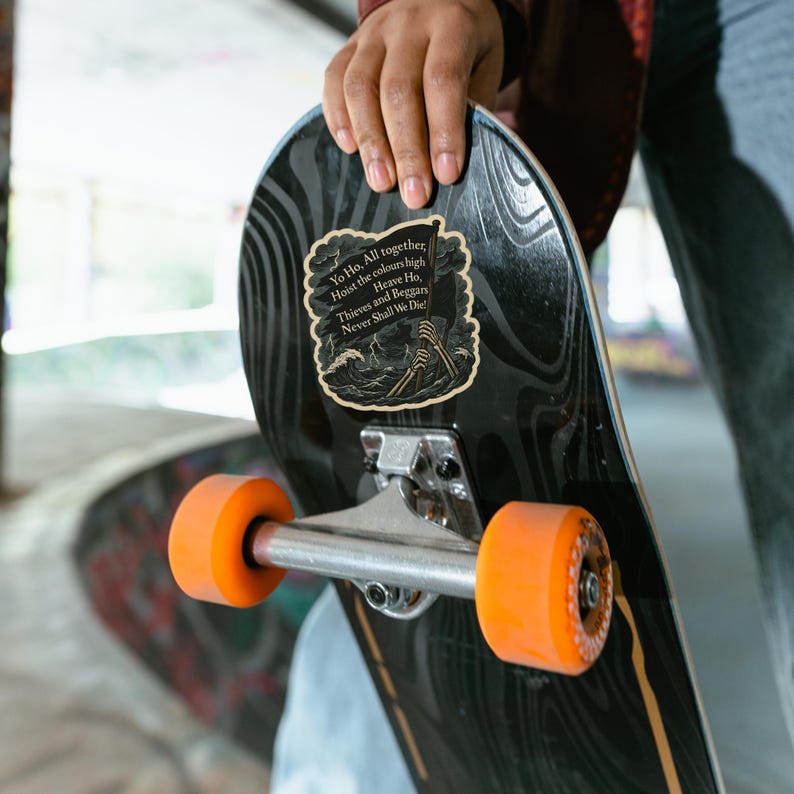 May include: A black skateboard with orange wheels. A sticker on the board features a pirate-themed design with the text "Yo Ho. All together, Hoist the colours high, Heave Ho, Thieves and Beggary Never Shall We Die!"