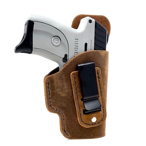 May include: A brown leather holster with a black clip for a small silver handgun. The gun has the word "RUGER" printed on the side.