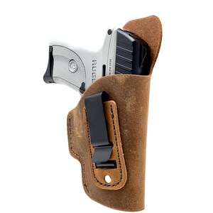 May include: A brown leather holster with a black clip for a Ruger LCP pistol. The holster has a distressed look and is designed for concealed carry.