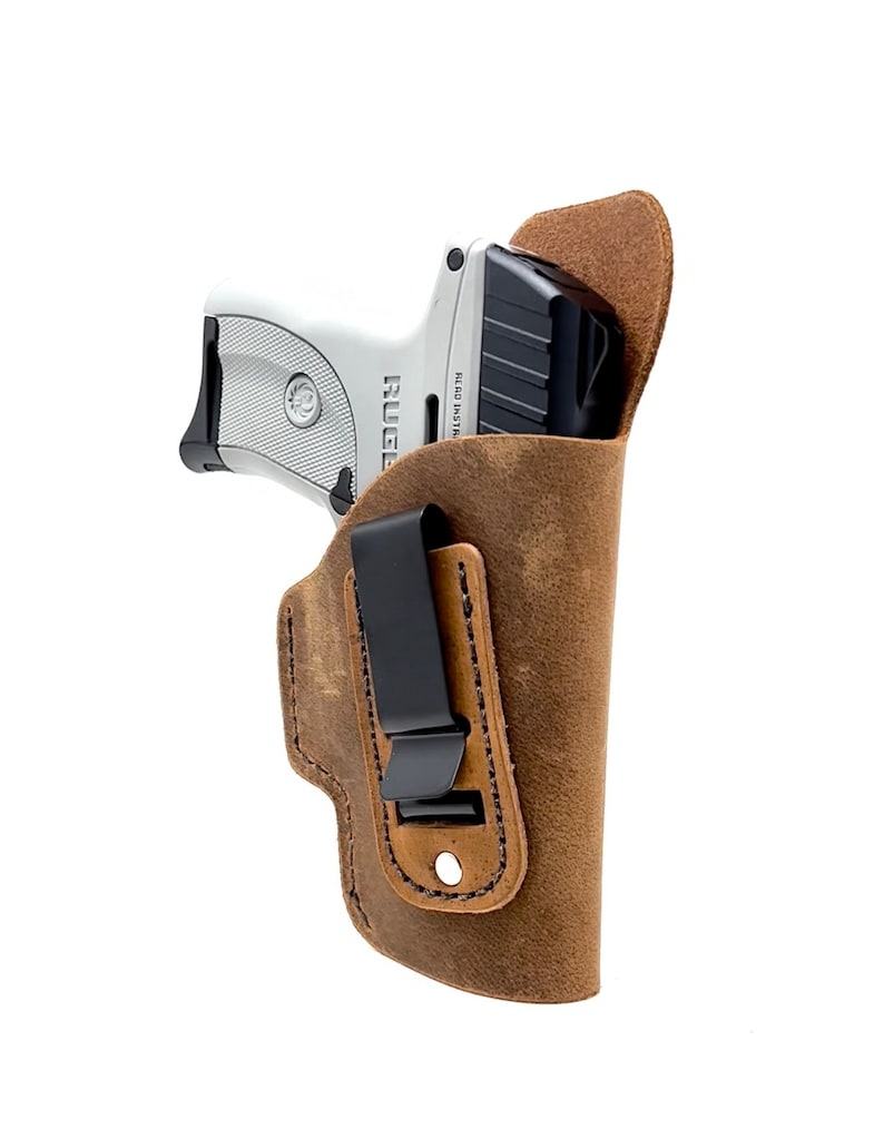 May include: A brown leather holster with a black clip for a Ruger LCP pistol. The holster has a distressed look and is designed for concealed carry.
