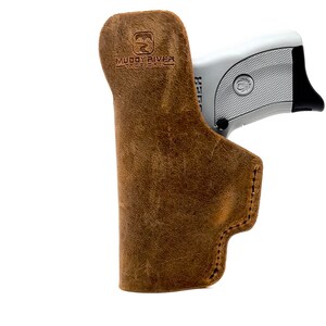 May include: A brown leather holster with a gun inside. The holster has the text "Muddy River Tactical" embossed on the side.