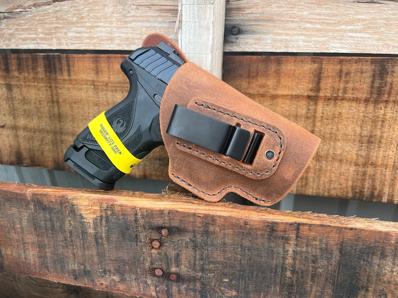 Puede incluir: Una funda de cuero marr&oacute;n con un clip de metal negro para una pistola. La funda est&aacute; dise&ntilde;ada para adaptarse a una pistola Ruger Lite Rack Security-9.