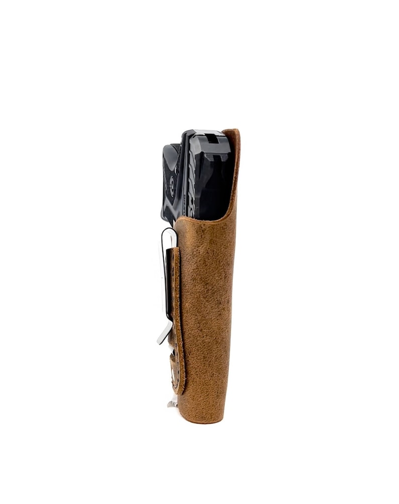 Puede incluir: Una funda de cuero marr&oacute;n con una pistola negra en su interior. La funda tiene un clip de metal en el lateral.