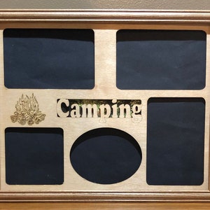 May include: A wooden picture frame with a cutout design for five photos. The frame has a light brown stain and the word "Camping" is engraved in the center. A campfire design is engraved in the bottom left corner.