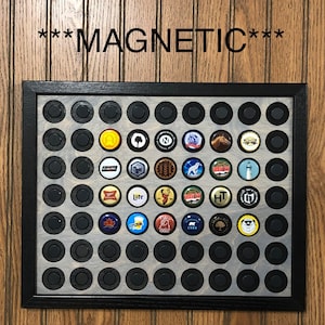 May include: A black framed magnetic board with a gray background and 64 round black circles. The circles are arranged in an 8x8 grid. The board is filled with bottle caps, each with a different design. The board has the word "MAGNETIC" printed in black letters at the top.