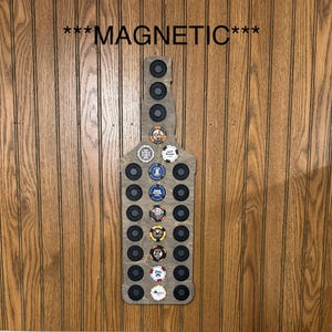 Puede incluir: Soporte magn&eacute;tico de madera con forma de botella con imanes negros y varios fichas de p&oacute;quer. El texto "MAGNETIC" est&aacute; encima del soporte. El soporte est&aacute; montado en una pared con paneles de madera.