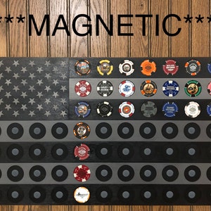 May include: A black wooden American flag with a gray and black striped design. The flag has 50 round spaces for poker chips. The spaces are filled with various poker chips with different designs. The text "***MAGNETIC***" is at the top of the flag.
