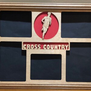 May include: Wooden shadow box with a light brown frame. The box has five openings with a dark blue background. A red circle features a cutout of a runner. The words "CROSS COUNTRY" are displayed in cutout letters.