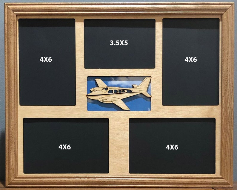 K&ouml;nnte beinhalten: Ein Bilderrahmen aus Holz mit f&uuml;nf &Ouml;ffnungen f&uuml;r Fotos. Der Rahmen hat einen Ausschnitt eines kleinen Flugzeugs in der Mitte. Die &Ouml;ffnungen sind mit den Ma&szlig;en 4x6 und 3.5x5 beschriftet.