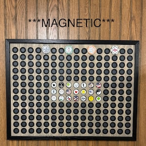 May include: A black framed magnetic display board with a light wood grain background. The board is filled with small, round, gray magnets. Several golf ball markers with various designs are attached to the board. The word "MAGNETIC" is written across the top.