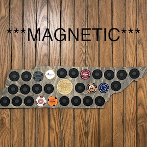 May include: A wooden Tennessee state-shaped magnetic bottle cap holder with 24 black circles for bottle caps. The holder has a brown stain and is decorated with various bottle caps.