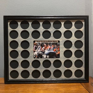 May include: A black wood frame with a gray wood background and 36 round holes for bottle caps. The frame has a 3.5 x 5 inch photo space with a photo of a group of people riding motorcycles. The text "Your 3.5 x 5 Photo Here" is printed on the photo space.