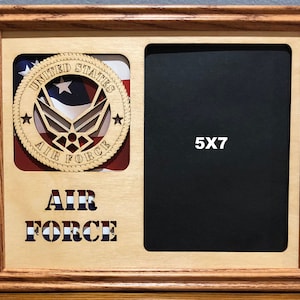 May include: A wooden picture frame with a 5x7 inch photo opening. The frame has a cutout of the United States Air Force emblem with the words "United States Air Force" around it. The frame also has the words "Air Force" in large letters below the photo opening.