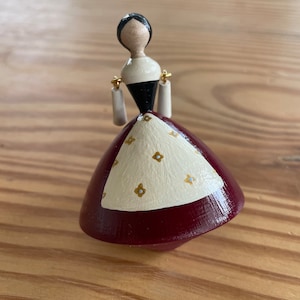 May include: A wooden spinning doll with black hair, a white face, and a red and white dress with gold accents.