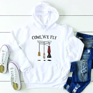 May include: White hoodie with a black graphic of three broomsticks hanging from a wire with the text "Come, We Fly".