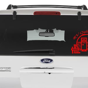 May include: A red vinyl sticker on the back window of a silver SUV. The sticker features a stylized illustration of a camper trailer with the text "RV Quilters" above it.