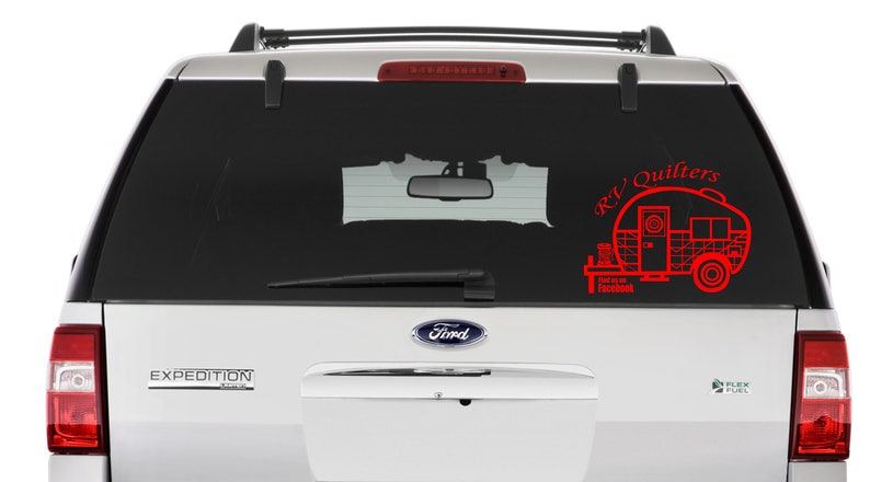 May include: A red vinyl sticker on the back window of a silver SUV. The sticker features a stylized illustration of a camper trailer with the text "RV Quilters" above it.