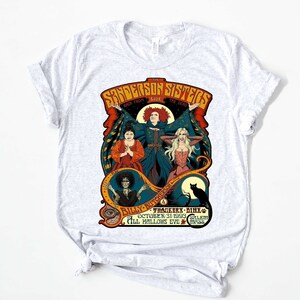 Pu&ograve; includere: Una maglietta bianca con una grafica in stile vintage delle sorelle Sanderson del film Hocus Pocus. La grafica presenta le tre sorelle nei loro costumi iconici, con il testo "The Sanderson Sisters" e "Back from the Dead" sopra di loro. Il testo "Billy Butcherson", "Thackeray Binx", "October 31, 1993", "Salem" e "All Hallows Eve Mass" &egrave; sotto le sorelle.