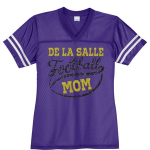 May include: Purple football jersey with white stripes on the sleeves. The jersey has gold glitter text that says "De La Salle Football Mom" with a black and gold glitter football graphic.
