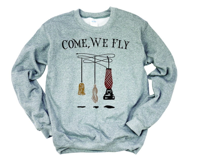 May include: A gray sweatshirt with the text "COME, WE FLY" printed on the front. The text is in black and is surrounded by three broomsticks, one of which is red and the other two are brown and beige.