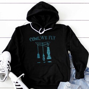 May include: Black hooded sweatshirt with a teal blue graphic that says "COME, WE FLY" and a design of three teal blue hanging lamps.