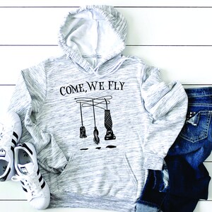 May include: A gray and white hooded sweatshirt with the text "COME, WE FLY" printed on the front. The text is in black and there is a graphic of a broom and a vacuum cleaner hanging from a string.