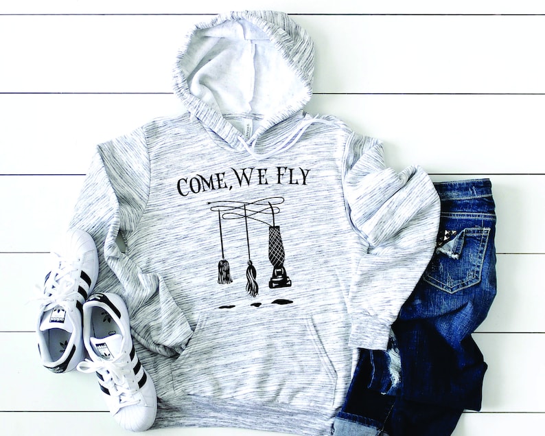 May include: A gray and white hooded sweatshirt with the text "COME, WE FLY" printed on the front. The text is in black and there is a graphic of a broom and a vacuum cleaner hanging from a string.