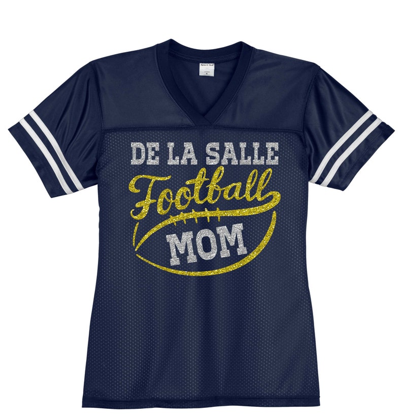 May include: Navy blue football jersey with white stripes on the sleeves. The jersey has gold glitter lettering that says "De La Salle Football Mom" with a gold glitter football graphic.