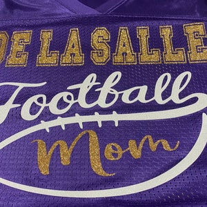 May include: Purple jersey with gold glitter lettering that reads "De La Salle Football Mom" with a white football graphic.