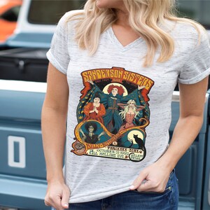 Pu&ograve; includere: Una maglietta bianca con una grafica in stile vintage delle sorelle Sanderson del film Hocus Pocus. La grafica presenta le sorelle nei loro costumi iconici, con il testo "The Sanderson Sisters" e "Back From The Dead" sopra di loro. Il testo "Billy Butcherson" e "Thacker -  Hinx" &egrave; sotto le sorelle. Il testo "October 31, 1993" e "All Hallows Eve" &egrave; nella parte inferiore della grafica.