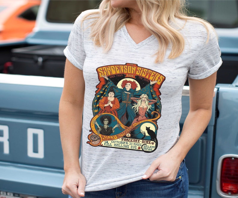 Pu&ograve; includere: Una maglietta bianca con una grafica in stile vintage delle sorelle Sanderson del film Hocus Pocus. La grafica presenta le sorelle nei loro costumi iconici, con il testo "The Sanderson Sisters" e "Back From The Dead" sopra di loro. Il testo "Billy Butcherson" e "Thacker -  Hinx" &egrave; sotto le sorelle. Il testo "October 31, 1993" e "All Hallows Eve" &egrave; nella parte inferiore della grafica.