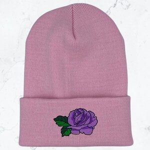 May include: A pink knitted beanie with a purple embroidered rose on the cuff.