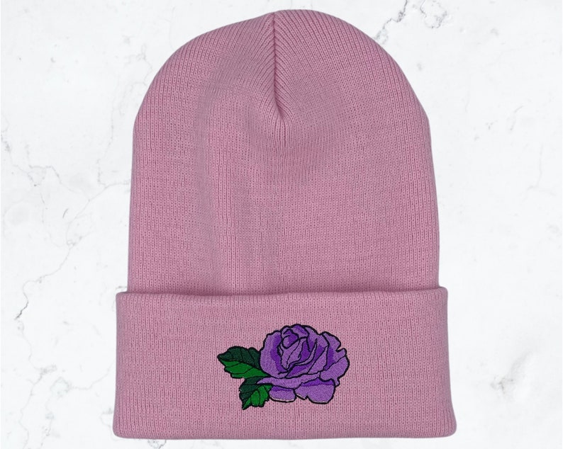 May include: A pink knitted beanie with a purple embroidered rose on the cuff.
