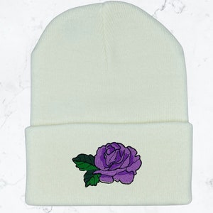 May include: White knitted beanie with a purple embroidered rose on the front.