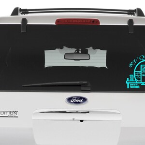 May include: A white SUV with a teal blue decal on the back window. The decal features a camper trailer with the text "RV Quilters" and "Find us on Facebook".