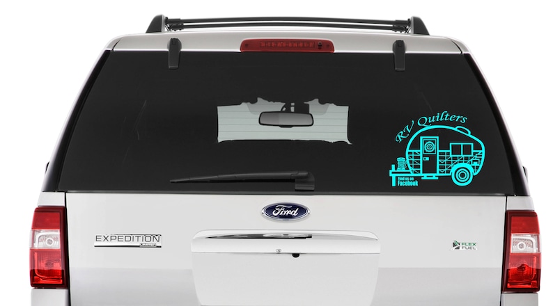 May include: A white SUV with a teal blue decal on the back window. The decal features a camper trailer with the text "RV Quilters" and "Find us on Facebook".