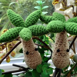 Puede incluir: Dos palmeras de crochet con troncos marrones y hojas verdes. Los árboles tienen caras sonrientes con ojos negros.