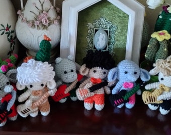 May include: A group of nine crocheted animal figurines playing musical instruments. The animals include a rabbit, an elephant, a sheep, a hippopotamus, and four other sheep. The instruments include a guitar, a bass guitar, and a keyboard.