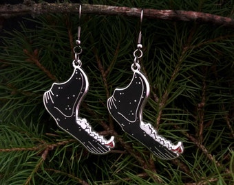 May include: A pair of silver earrings shaped like a wolf's jawbone with a black and white starry sky design. The earrings are hanging from a branch.