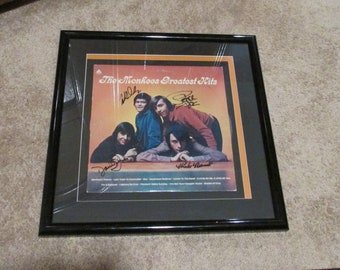 May include: A framed vinyl record album cover featuring a band called "The Monkees". The album title is "The Monkees Greatest Hits". The cover features a photo of the band members, and the album cover is signed by each band member.