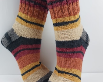 May include: Striped knit socks in shades of gray, black, beige, orange, and red. The socks are shown on a model's feet.
