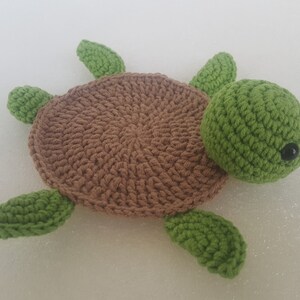 May include: A handmade crochet turtle in shades of brown and green. The turtle has a brown shell, green head, and four green flippers. The eyes are small black beads. This soft toy is perfect for a child's room.
