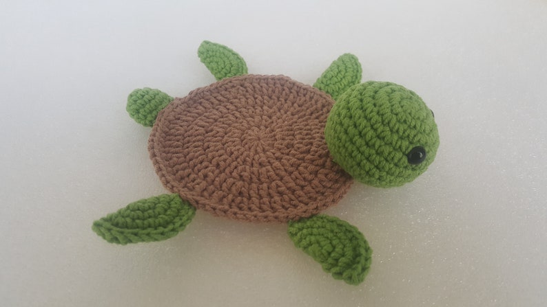 May include: A handmade crochet turtle in shades of brown and green. The turtle has a brown shell, green head, and four green flippers. The eyes are small black beads. This soft toy is perfect for a child's room.